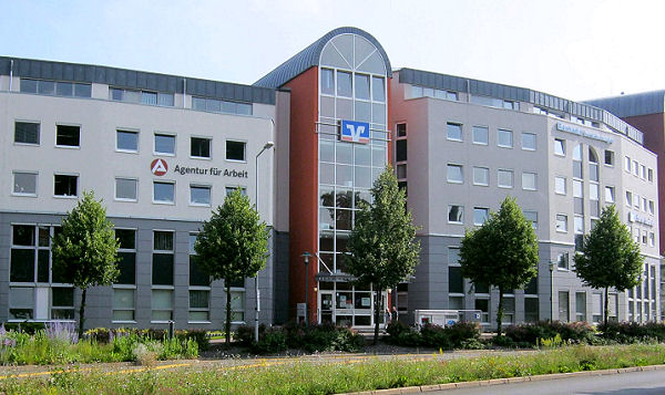 Bürogebäude in modernem Baustil mit gebogener Fassade, 5 gehwegbegleitende Bäume im Vordergrund