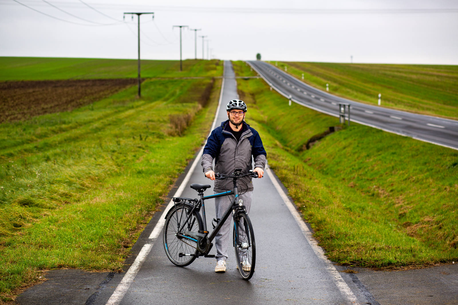 Junger Mann mit Fahrrad und Helm auf Radweg