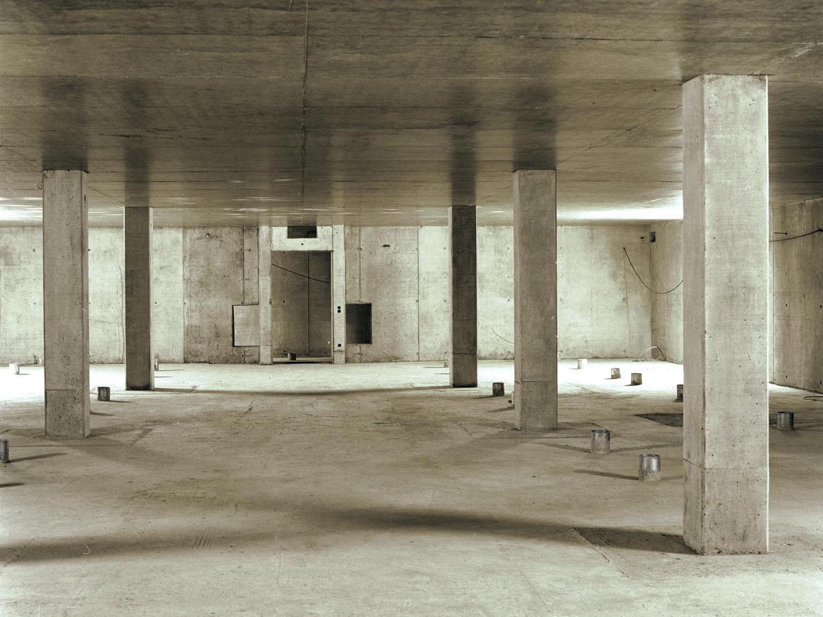 Ein kalter Raum, alle Decken, Böden und Wände sind aus Beton. Im Zentrum ist eine Öffnung, die später eine Tür wird. Es ist Rohbauzustand. Betonstützen stehen rechts und links vom Fokus mit rechteckigen Querschnitt.