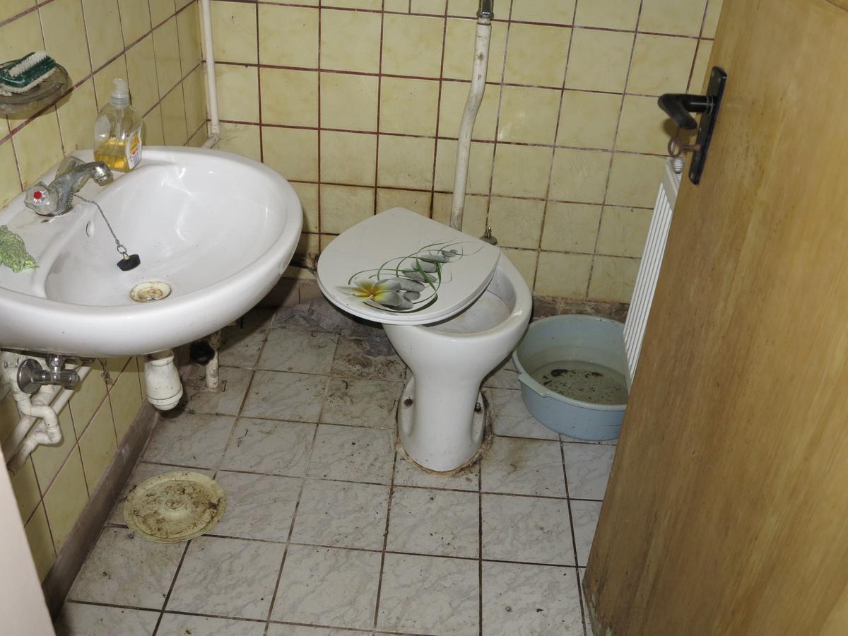 sehr stark verschmutztes und teilweise zerstörtes Badezimmer mit WC und Waschbecken; gefliest