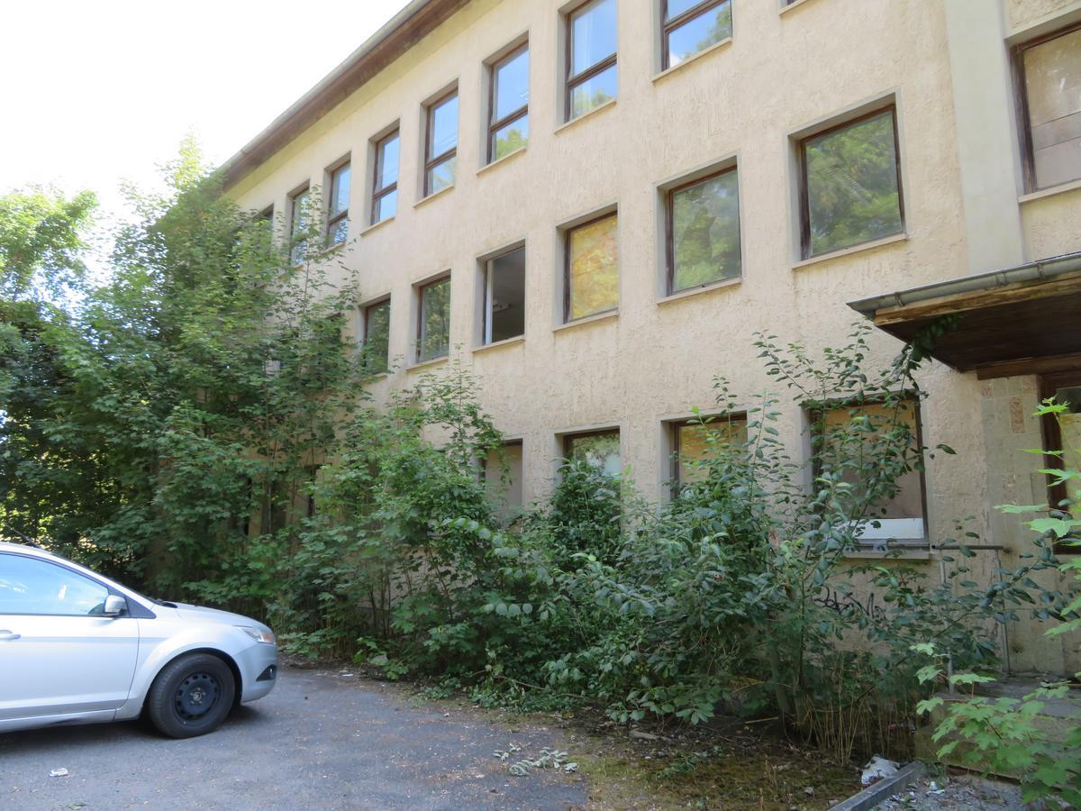 Vordere Teilansicht mit Grünwuchs teils auch vor den Fenstern und Stellplätzen