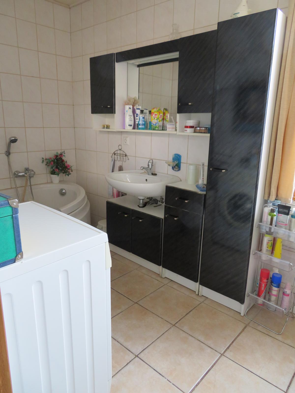gefliestes Bad mit Eckbadewann, Badschrank und Waschbecken, unberäumt