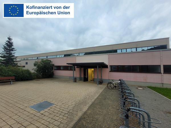 Sporthalle des Sportgymnasiums Jena - Ansicht auf Haupteingang, Zuwegung und Fahrradständer im Vordergrund mit EFRE-Logo
