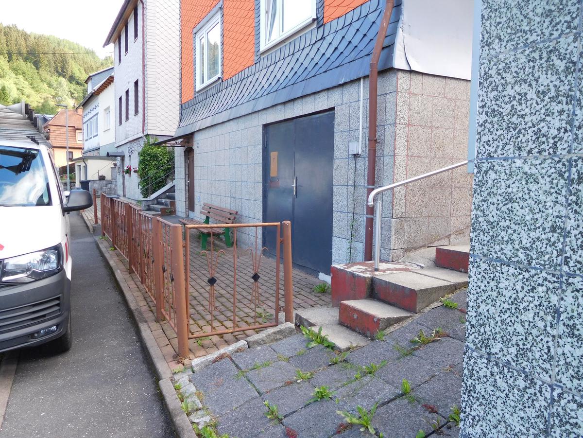 vor dem Haus ist eine ca. 1,50 m breite, gepflasterte Fläche auf Hauslänge eingezäunt, davor ein schmaler Gehweg
