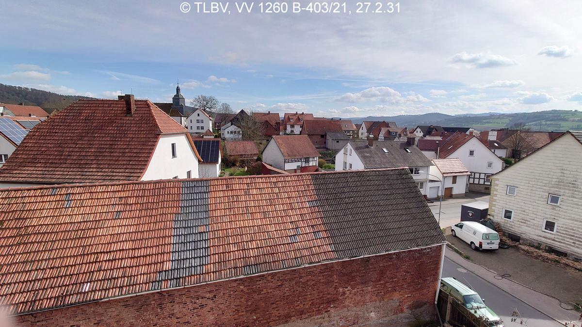 Blick über den Ort, im Vordergrund Dächer und Kirche, im Hintergrund leichte Bergzüge