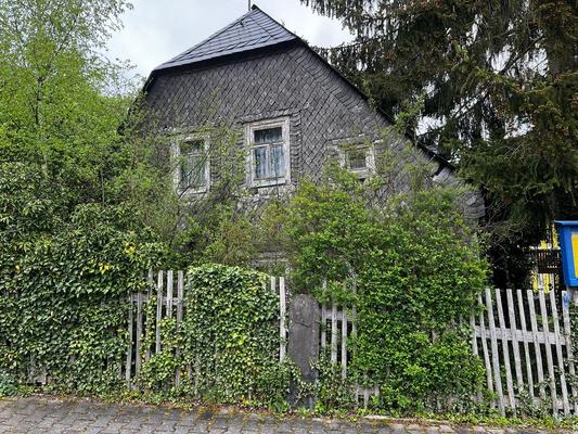 Blick auf ein giebelständiges Haus mit Fassadenschindeln und von Efeu und weiterem Aufwuchs umwuchert