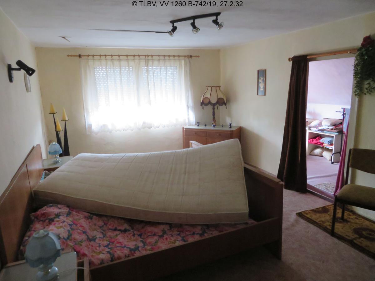 Schlafzimmer, unberäumt, ein großes Fenster mit heruntergelassener Außenjalousie