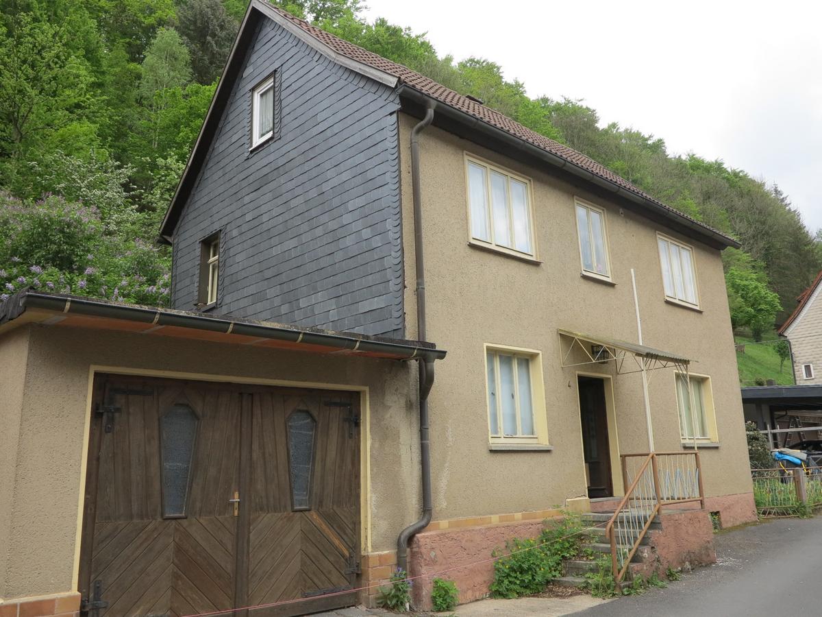 Straßenansicht des zweigeschossigen Wohnhauses mit Satteldach und westlichem Garagenanbau; Straßenfron mit 3 Fenstern im 1. OG, sowie 2 Fenstern und des Hauseingangs im EG, Hauseingang mit 5 Stufen und EIngangsvordach