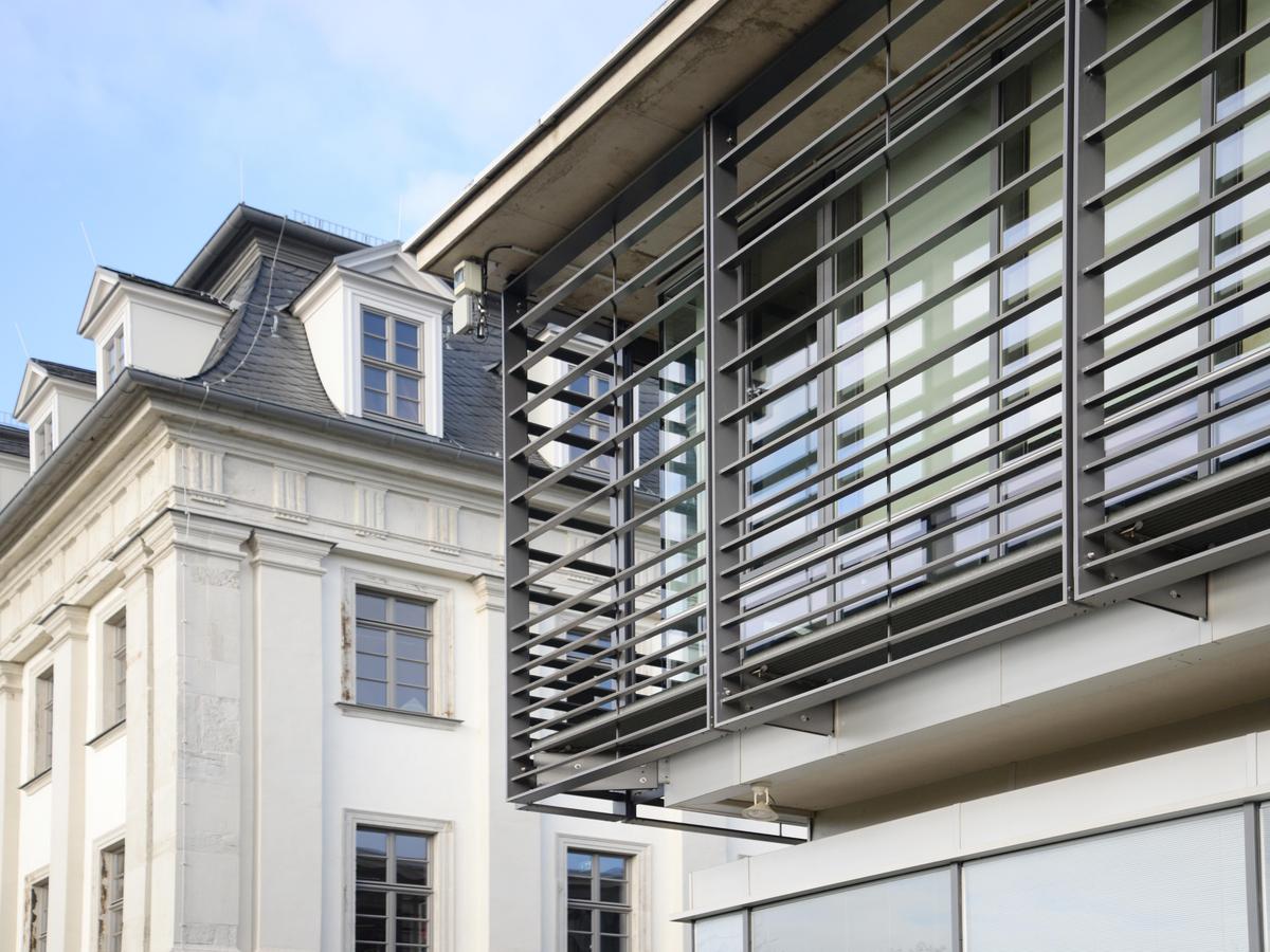 Detailfoto der modernen Neubaufassade mit horizontalen Lamellen und im Hintergrund Barockfassade des Schloss Tinz in Kontrast.