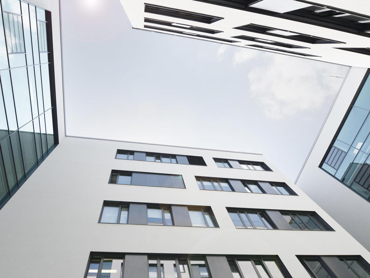 Foto mit Blickrichtung Himmel, leichte Wolken, an allen Bilderrändern Gebäudewände, mindestens vier Geschoss, weiße Putzfassaden mit schwarzen Fensterflächen.
