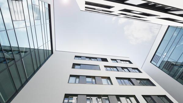 Foto mit Blickrichtung Himmel, leichte Wolken, an allen Bilderrändern Gebäudewände, mindestens vier Geschoss, weiße Putzfassaden mit schwarzen Fensterflächen.