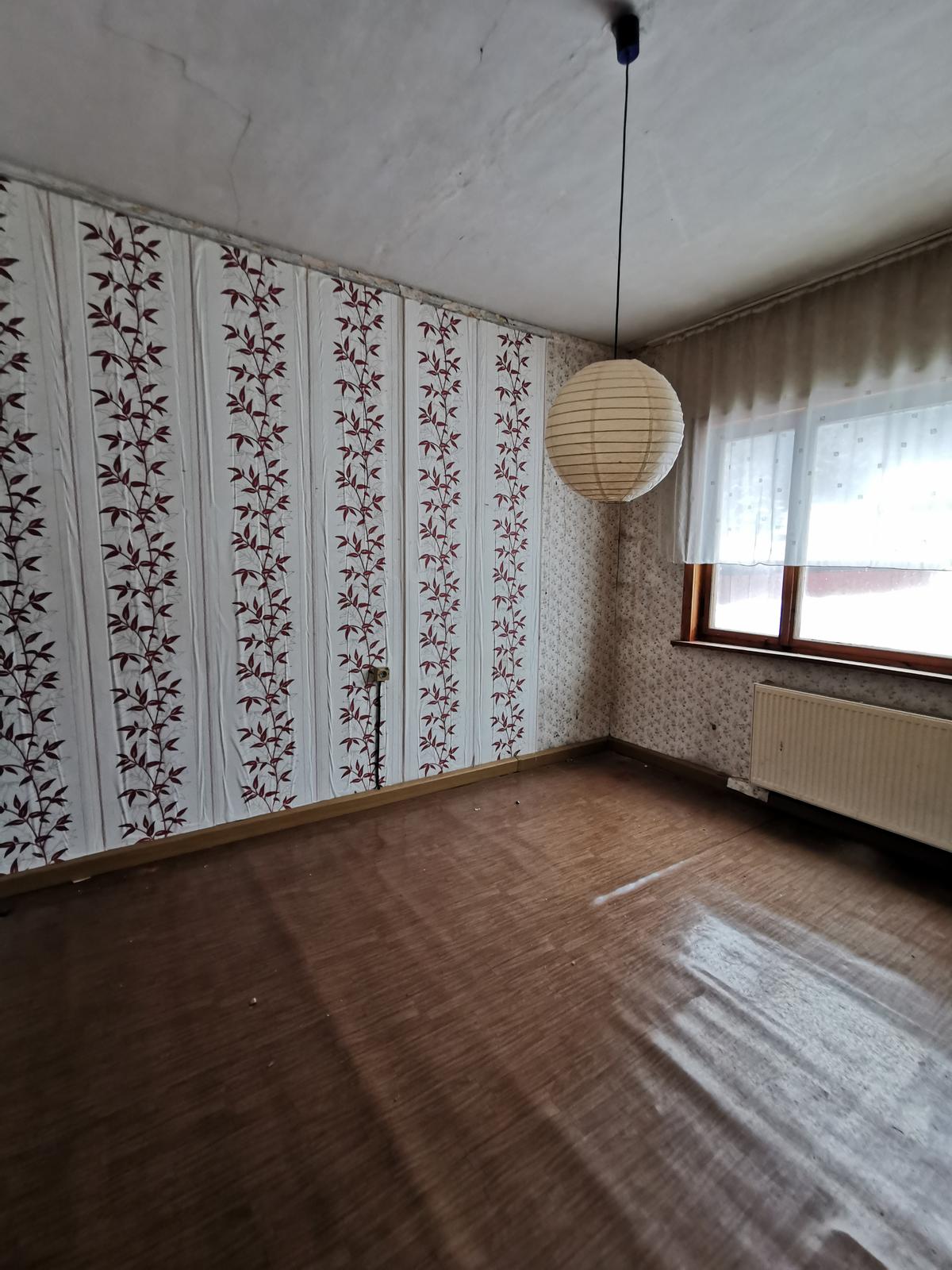 leeres Zimmer, ein Fenster, ein Heizkörper; Fußbodenbelag sowie Wand und Deckenanstrich sind verschlissen