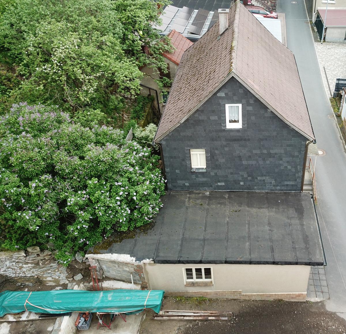 Drohnenaufnahme der westl. Giebelseite mit Garagenanbau; im DG und im 1. OG je ein Fenster; Giebelfassade mit Schindeln versehen