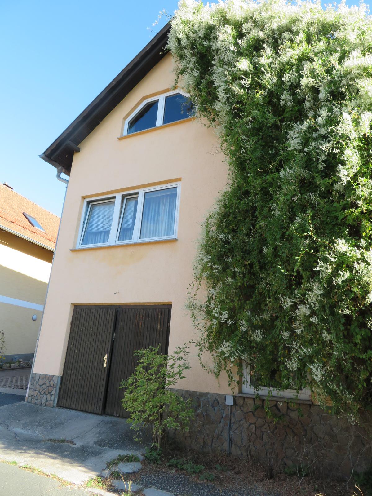 Straßenansicht; giebelständig; Garagentor im EG; im 1 OG ein dreiflügeliges Fenster, im ausgebauten DG ein halbrundes Fenster; rechte Fassade verwachsen mit Knöterich