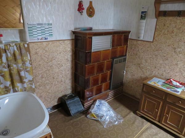 Raum mit Waschbecken und großem Kachelofen sowie diversen Kleinmöbeln