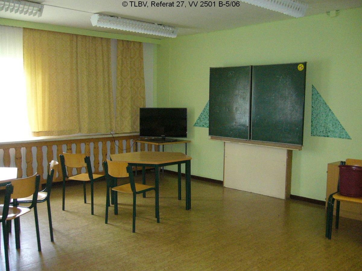 Zimmer mit Schultafel und Tischen und Stühlen