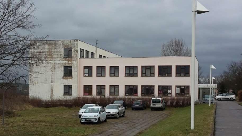 über eine Wiese Vordergrund fotografiertes Schulgebäude, Quergebäude zweigeschossig, Längsgebäude dreigeschossig