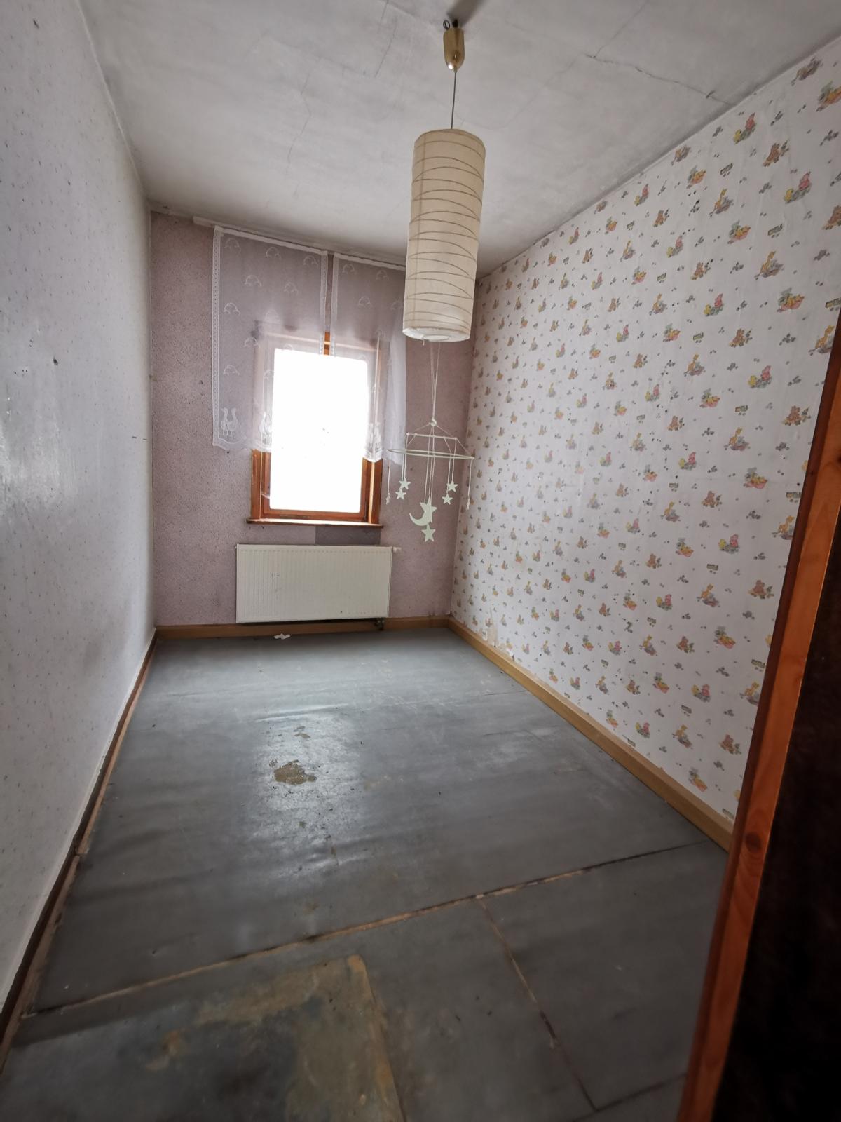 sehr schmales Zimmer, an Stirnseite ein Fenster , darunter ein Heizkörper; Fußboden verschlissen, eine Seite mit kindgerechter Tapete versehen