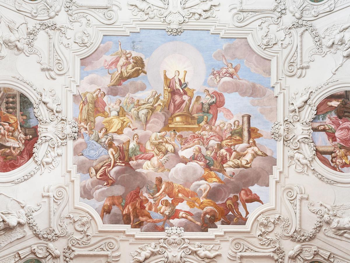 Deckenfresko des Barocksaals, aufwendige weiße Stuckarbeiten. Ein zentrales Gemälde mit Menschen im Himmel auf Wolken, im Zentrum der heilige Jesus. Rechts und links davon kleinere Gemälde mit Szenen aus der Bibel.