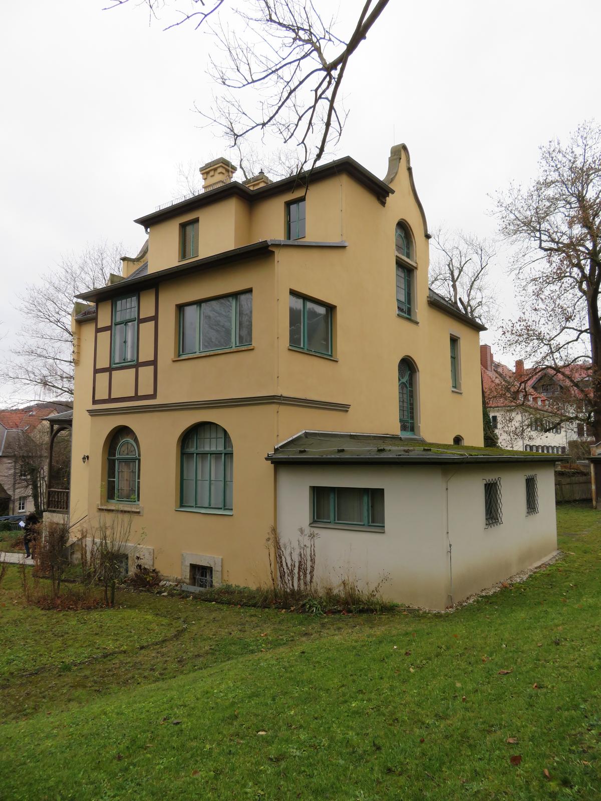 Blick auf Villa mit durchbrochener Fassade und hinterem Anbau auf großzügigem Grundstück