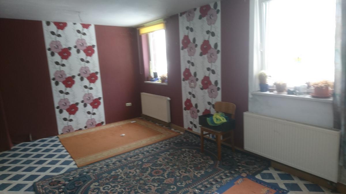 leeres Zimmer mit vielen Teppichen, zwei Fenstern, zwei Heizkörpern und kontrastreicher Tapete