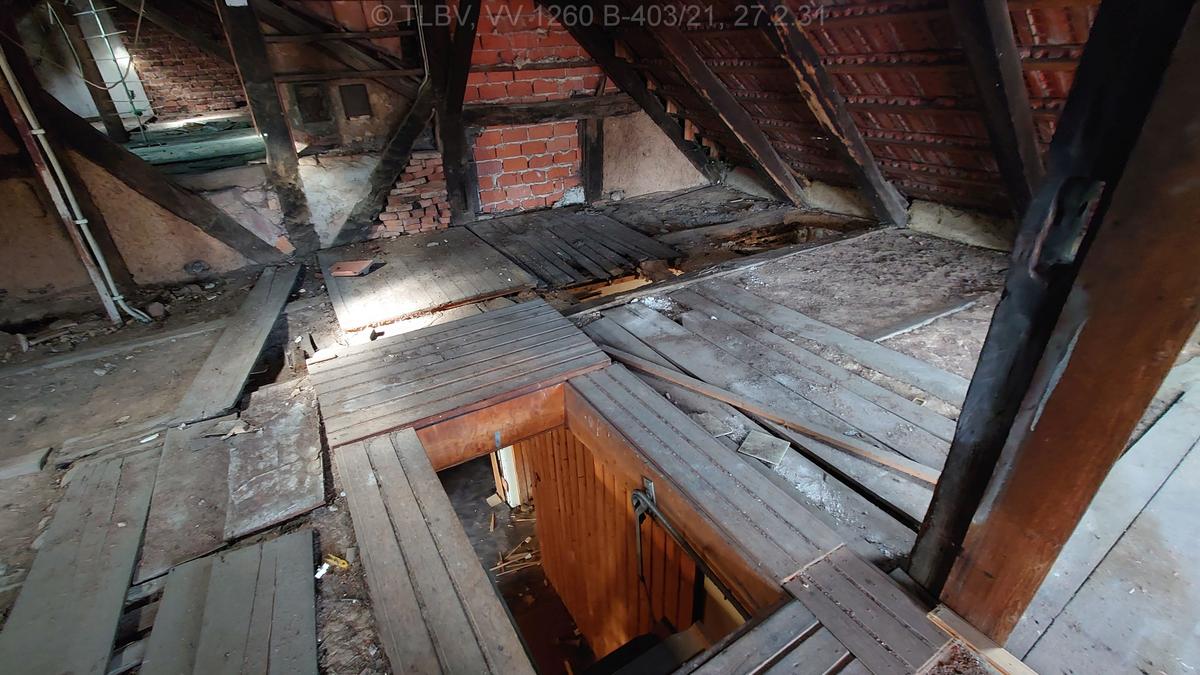 im Dachstuhl stehend mit Blick auf den Fußboden mit Luke zum OG; Fußboden als lose Schüttung, teilweise mit Holzplanken bedeckt; Fachwerkgiebel - Ausfachungen mit unterschiedlichem Material
