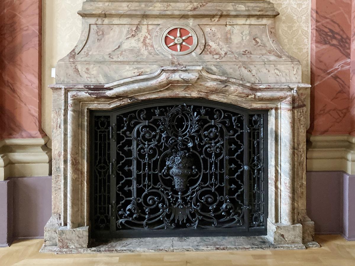Kamin im Stil des Barock im Barocksaal mit Erfurter Wappenrad oberhalb der Brennkammer. Schmiedeeisernes schwarzes Tor mit filigraner Gestaltung.