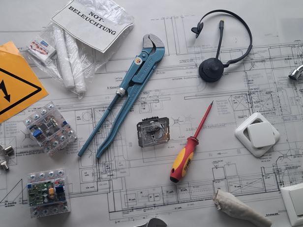 Auf einem ausgebreiteten technischen Gebäudeplan aus Papier liegen verschiedene Werkzeuge und Zubehörteile, die die Vielfalt das Themas technische Gebäudeausrüstung symbolisieren.