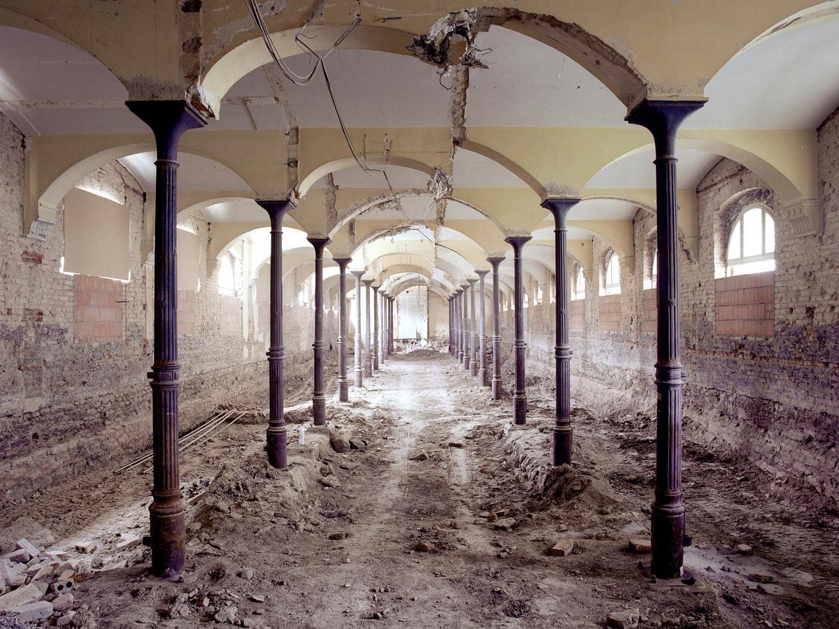 Zentralperspektive, rechts und links aufgereihte Stütze, die die Rundbogen stützen, diese sind immer beschädigt und optisch nicht funktionsfähig. Kein Putz an den Außenwänden. Die Fensters sind zur hälfte ausgemauert oder teilweise mit Karton geschlossen. Es gibt keinen Fußboden, hier liegt nur Schutt und Erdmaterial. Reifenspuren lassen vermuten, dass hier ein Auto durchgefahren ist.