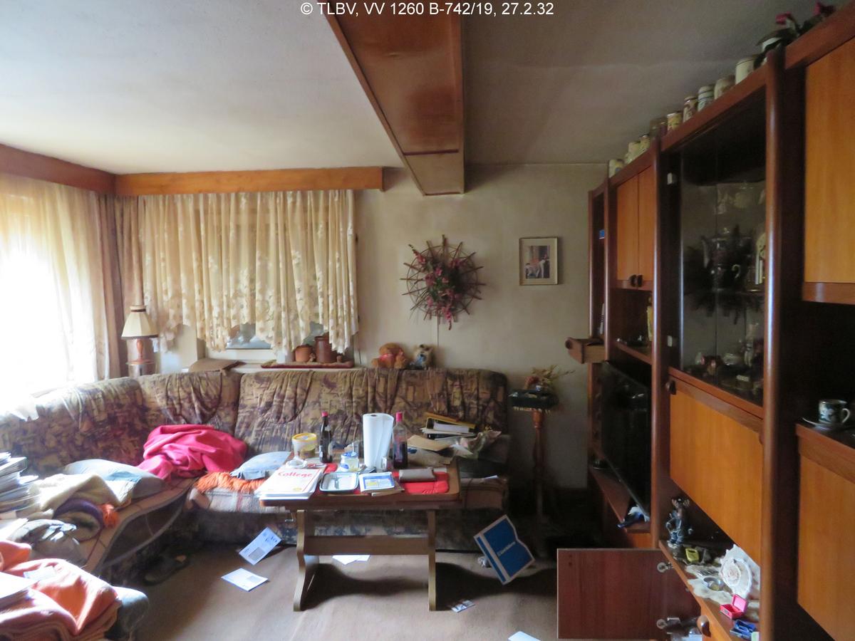 Wohnzimmer, unberäumt, Fußboden, Wände, Gardinen, stark verschlissen; zwei Fenster über Eck, teilweise Außenjalousien