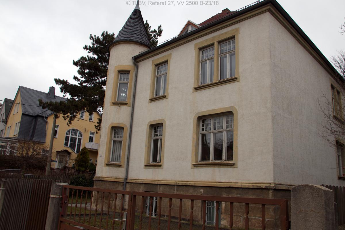 Außenansicht über Zufahrt mit Stellplatz im Vordergrund; Holzfensterrahmen mit abblätternder Farbe