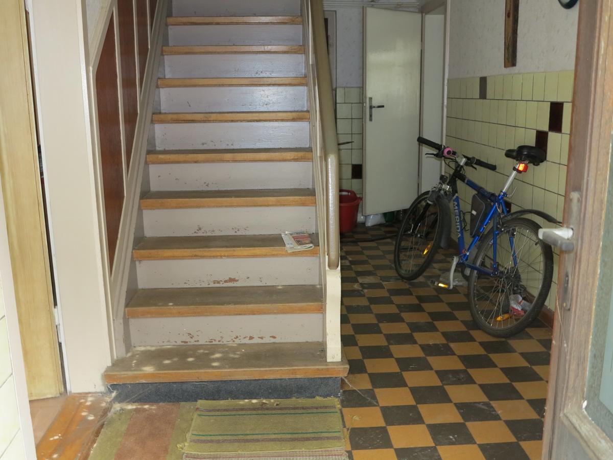 Blick hinter die Hauseingangstür in ein Treppenhaus; Fußboden schachbrettartig gefliest; Holztreppe ins 1. OG