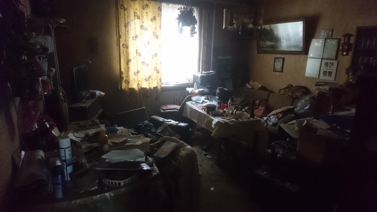 völlig vermülltes und verschmutztes Wohnzimmer, sehr düster, ein Fenster, ein Heizkörper