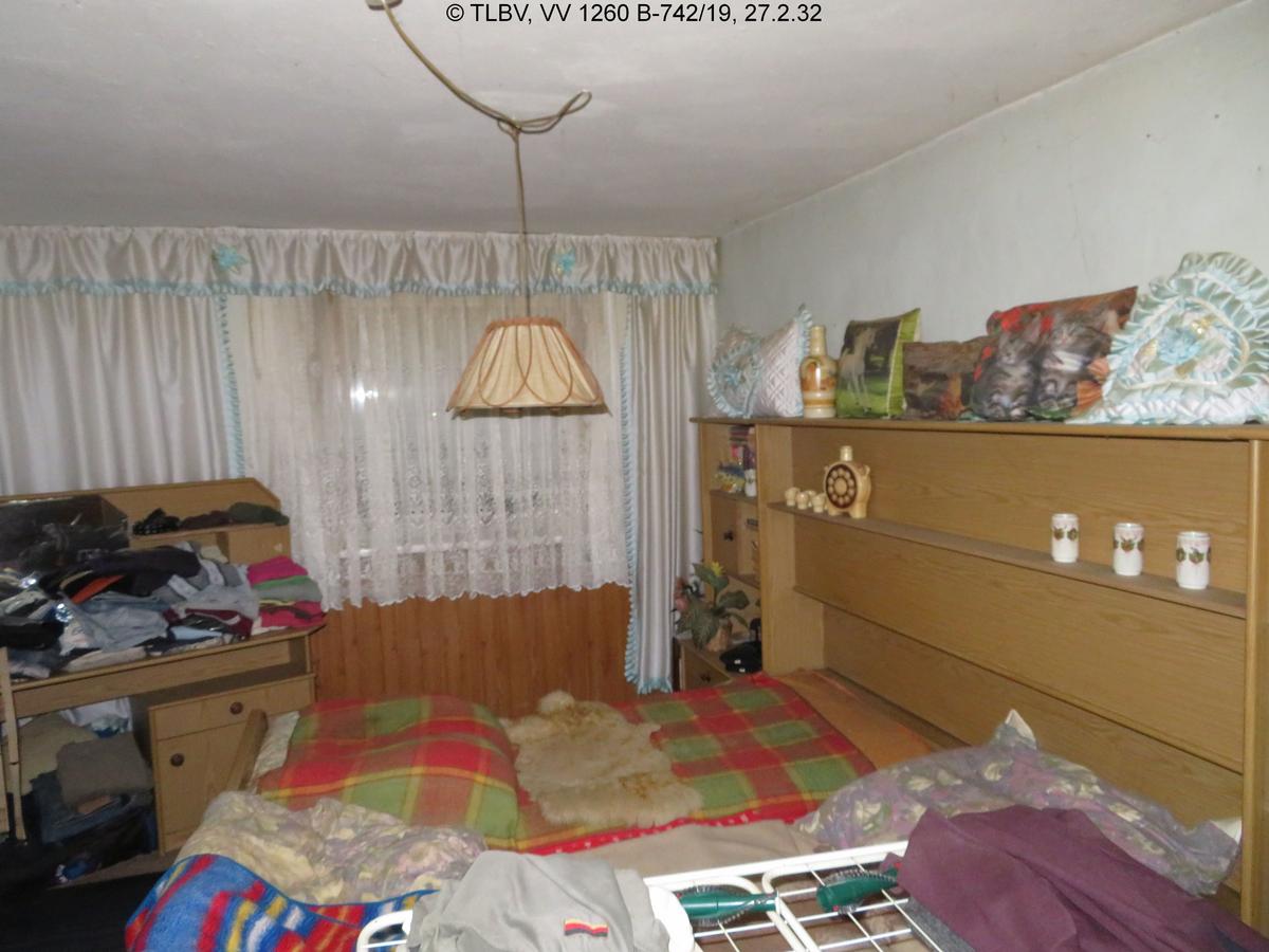 Schlafzimmer, vermüllt und verschmutzt, scheinbar niedrige Deckenhöhe, zwei Fenster mit heruntergelassenen Außenjalousien