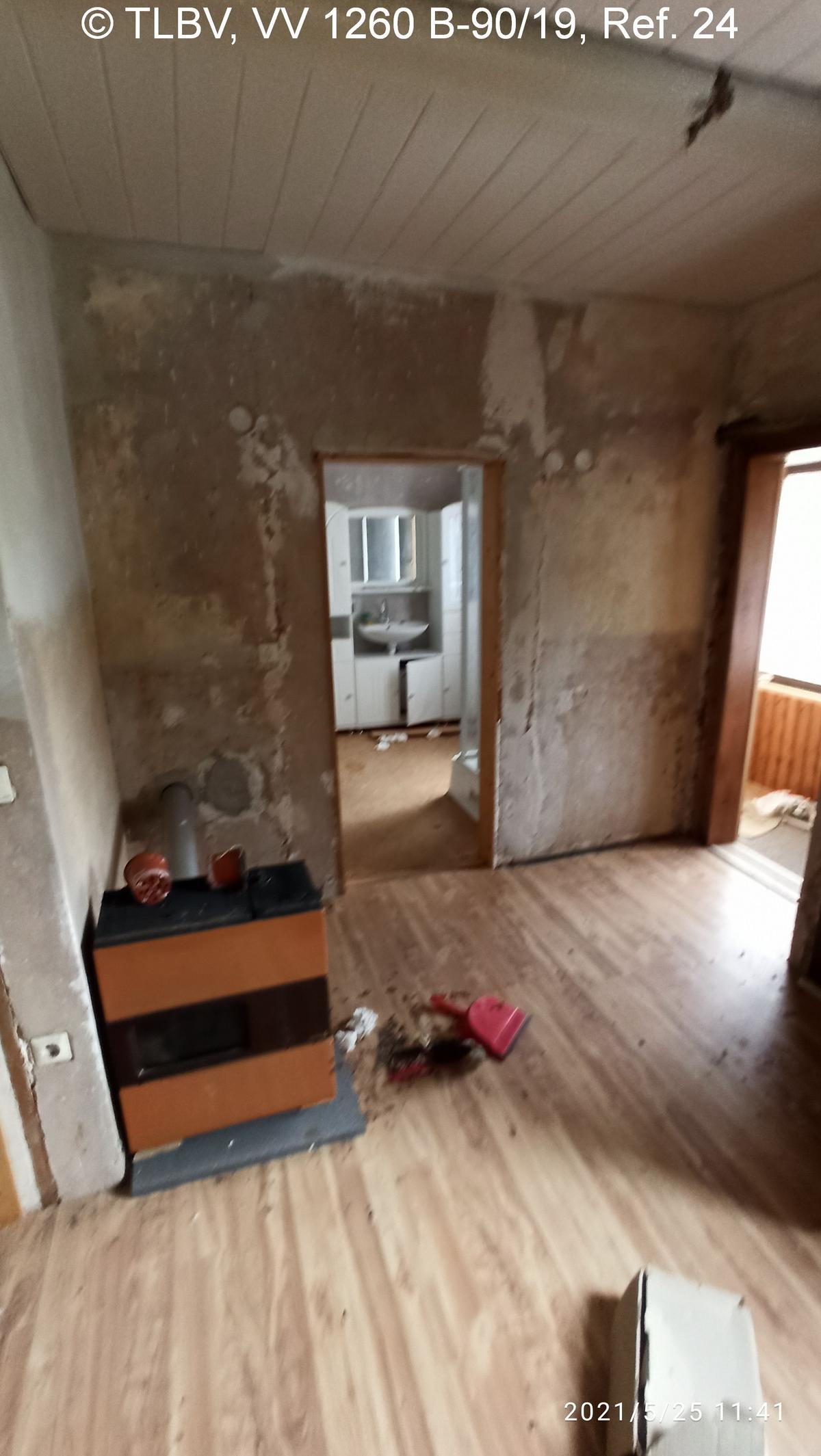 Durchgangszimmer mit Ofen, weiter Blick in ein Bad mit Dusche, Wände im Rohbauzustand