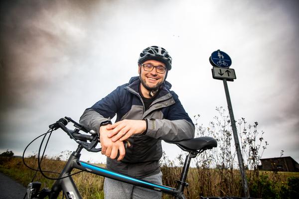 Junge Mann auf Fahrrad gelehnt, lächelt freundlich nach unten in die Kamera Junge Mann auf Fahrrad gelehnt, lächelt freundlich nach unten in die Kamera