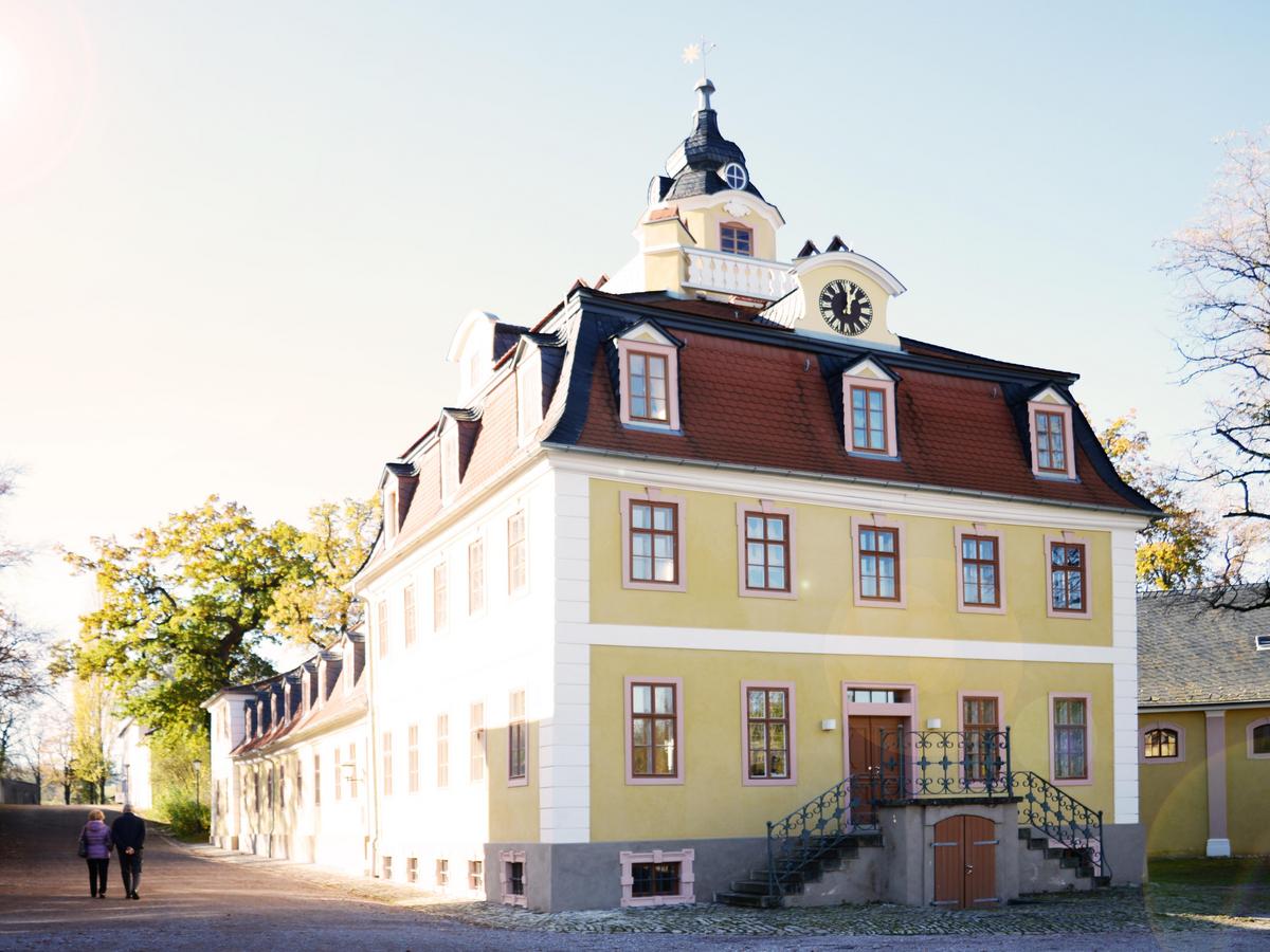 Turmhaus des Mozarthauses mit gelber Fassade, Rennaissance-Stil, rotes Mansarddach mit drei Gauben. Darüber thront der Turm, links führt ein Weg mit zwei Personen aus dem Bild.
