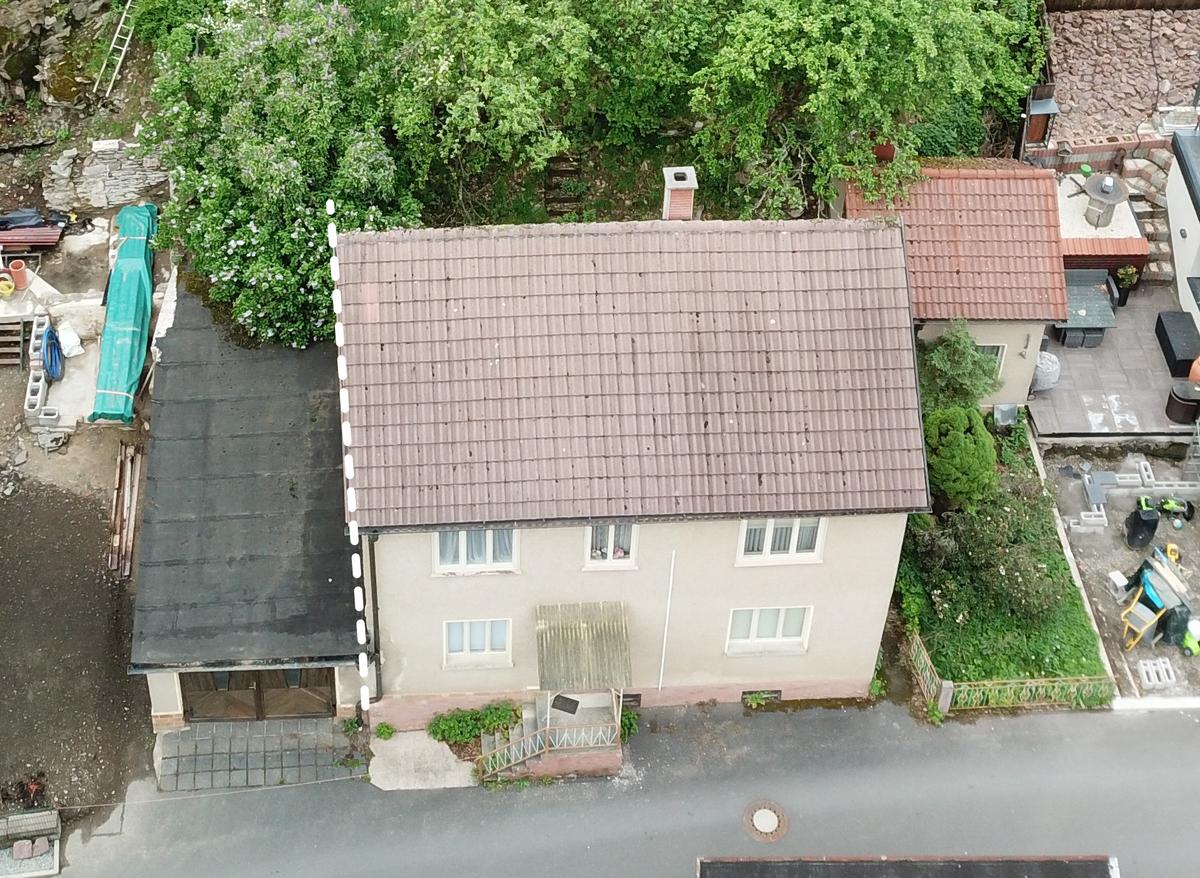 Drohnenaufnahme auf das Gesamtgrundstück; traufständiges Haus mit zwei Geschossen plus Satteldach, Garagenanbau, rückseitiger Baumbestand