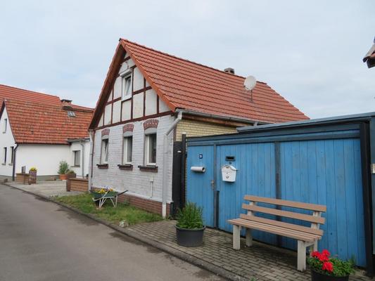 straßenseitige Ansicht eines giebelständigen Hauses; im Giebel Fachwerk; an Haus schließt sich eine blaue Torfahrt an